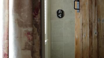 A bathroom with a wooden door, tiled walls, and a visible shower control panel.