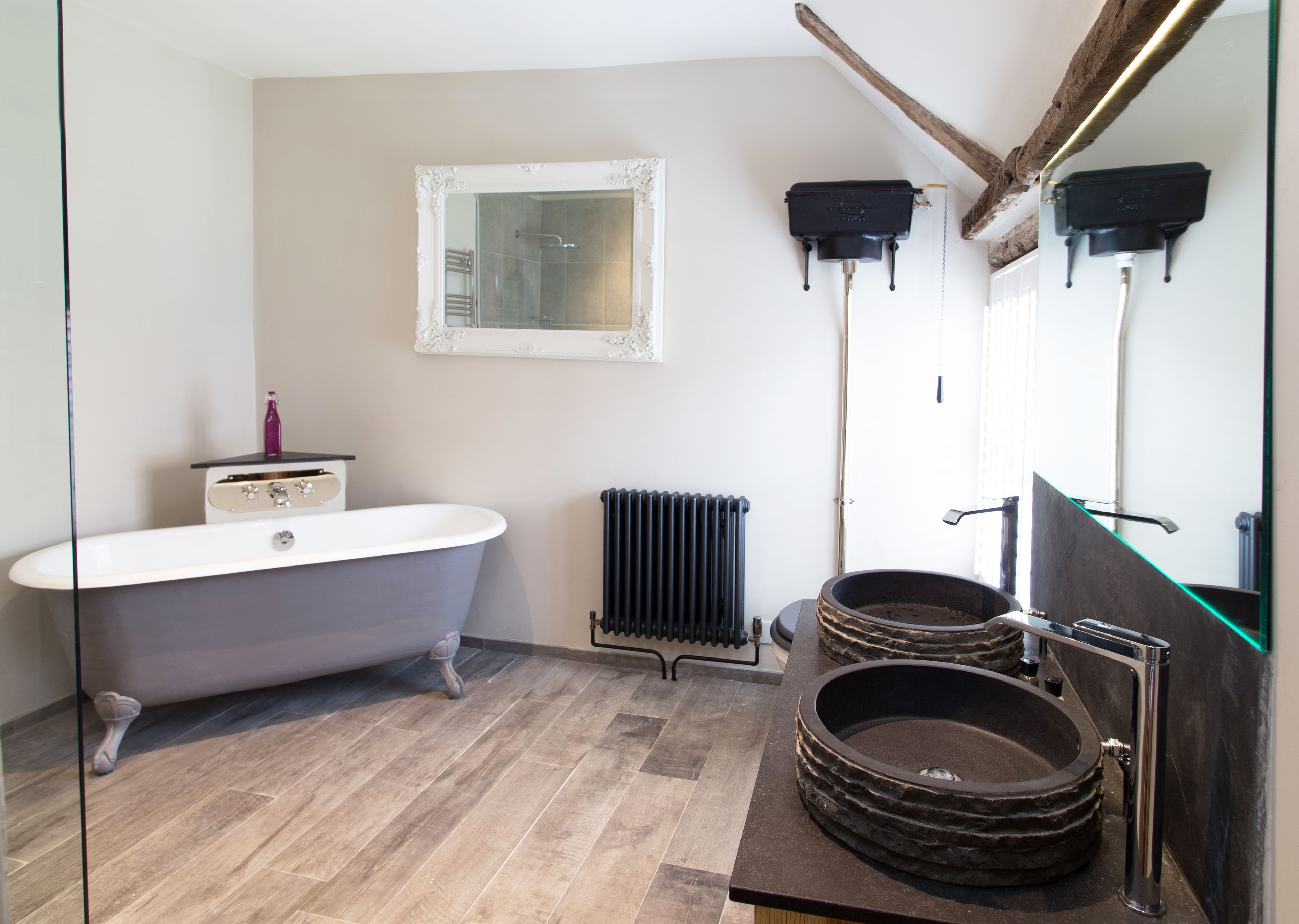 Une salle de bain dotée d’une baignoire sur pieds, d’un lavabo moderne avec un receveur en pierre, d’un radiateur et d’un miroir avec un cadre décoratif.