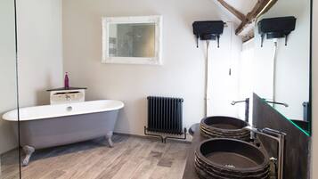 A bathroom with a freestanding bathtub, a modern sink with a stone basin, a radiator, and a mirror with a decorative frame.