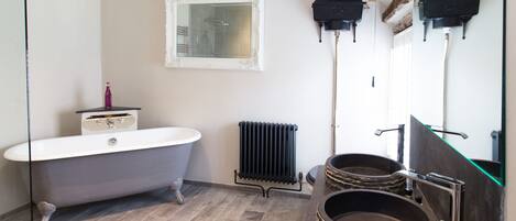 Une salle de bain dotée d’une baignoire sur pieds, d’un lavabo moderne avec un receveur en pierre, d’un radiateur et d’un miroir avec un cadre décoratif.