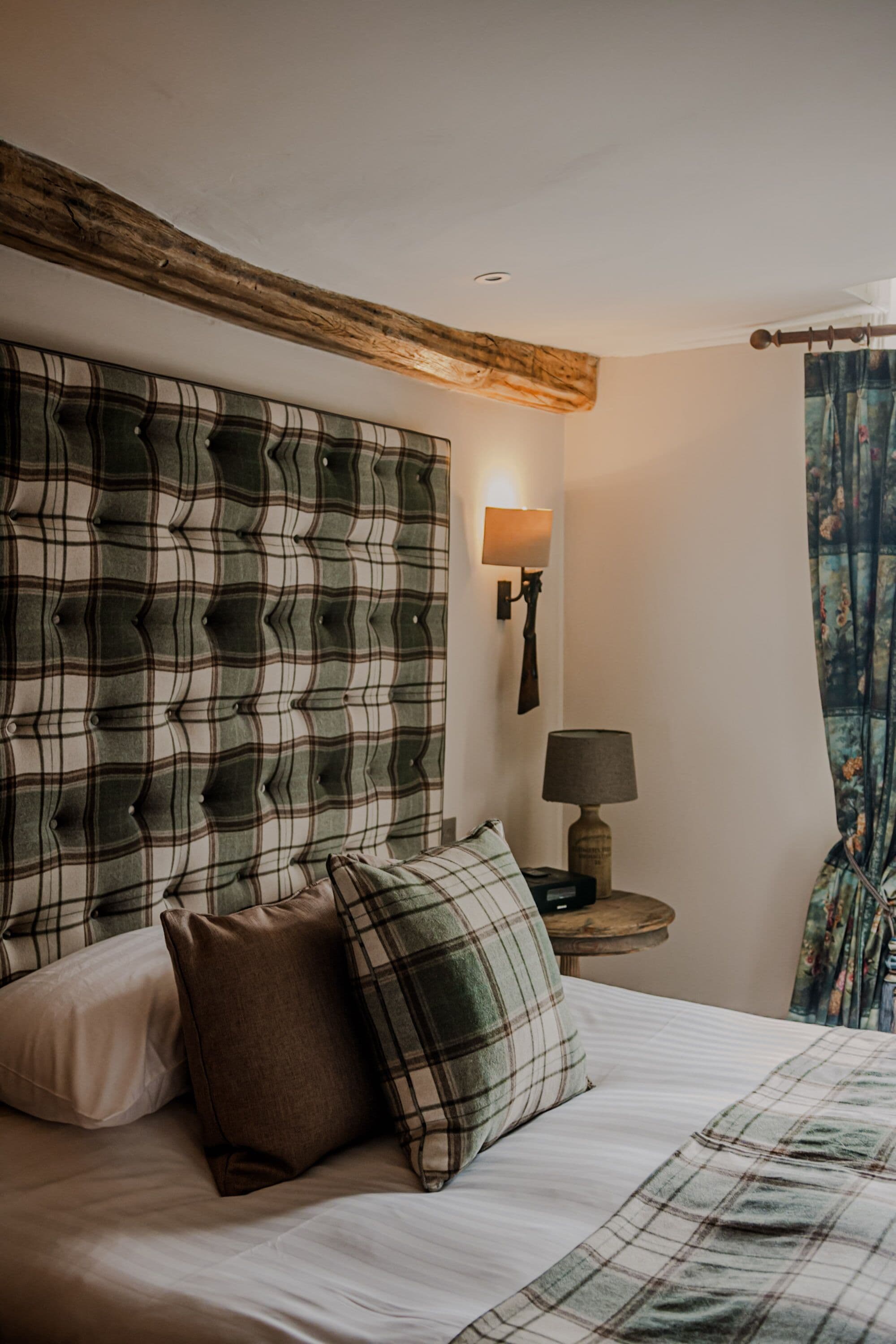 A bedroom with a plaid headboard, a bedside table with a lamp, and a bed with pillows.