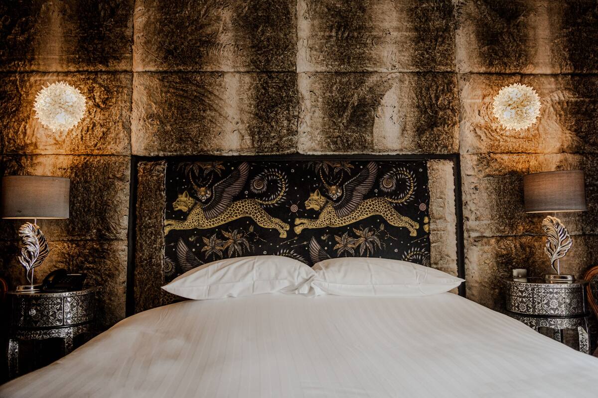 A bed with a decorative headboard, two bedside tables with lamps, and a wall with a textured pattern.