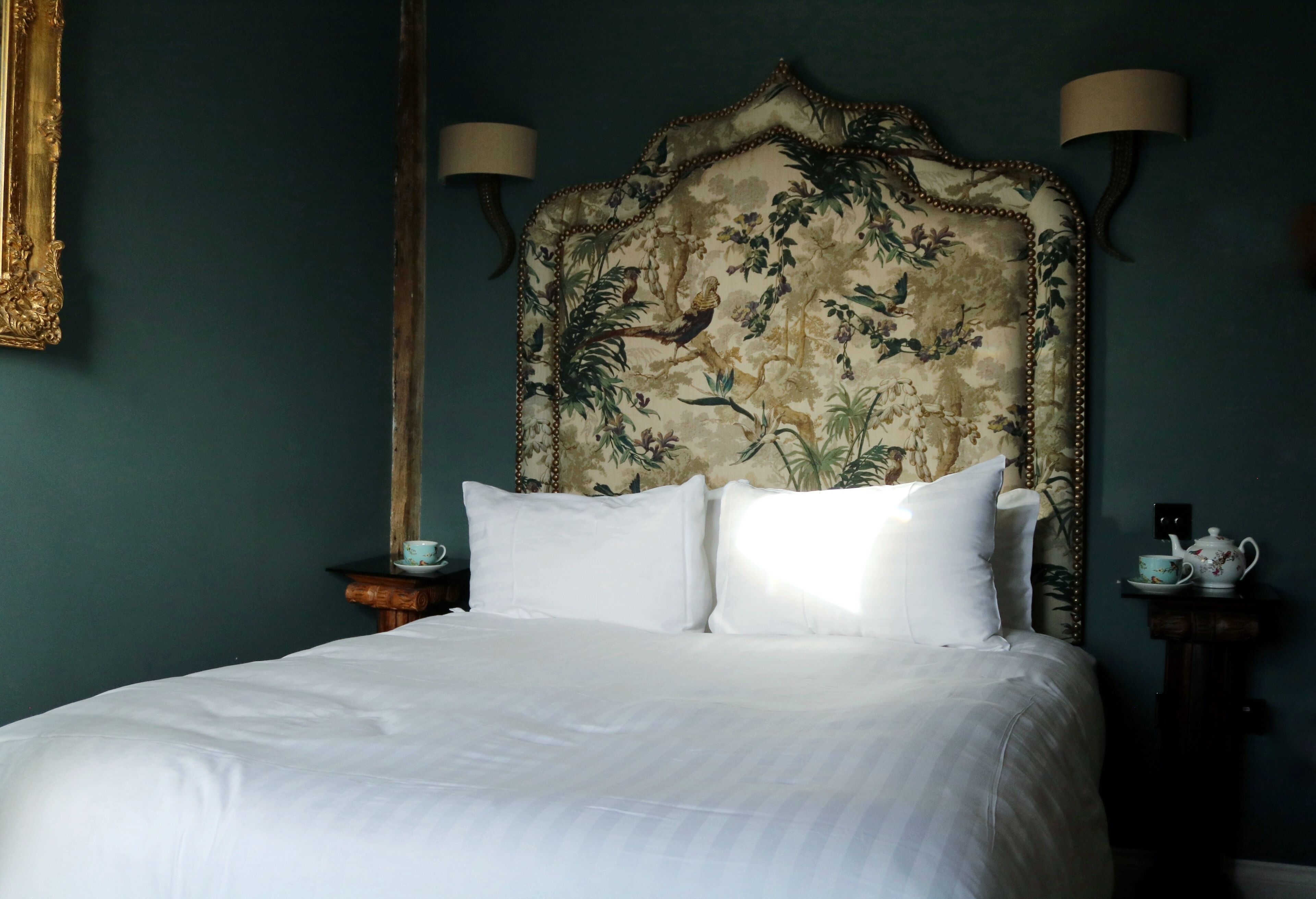 A neatly made bed with white linens, a floral headboard, and two bedside lamps.