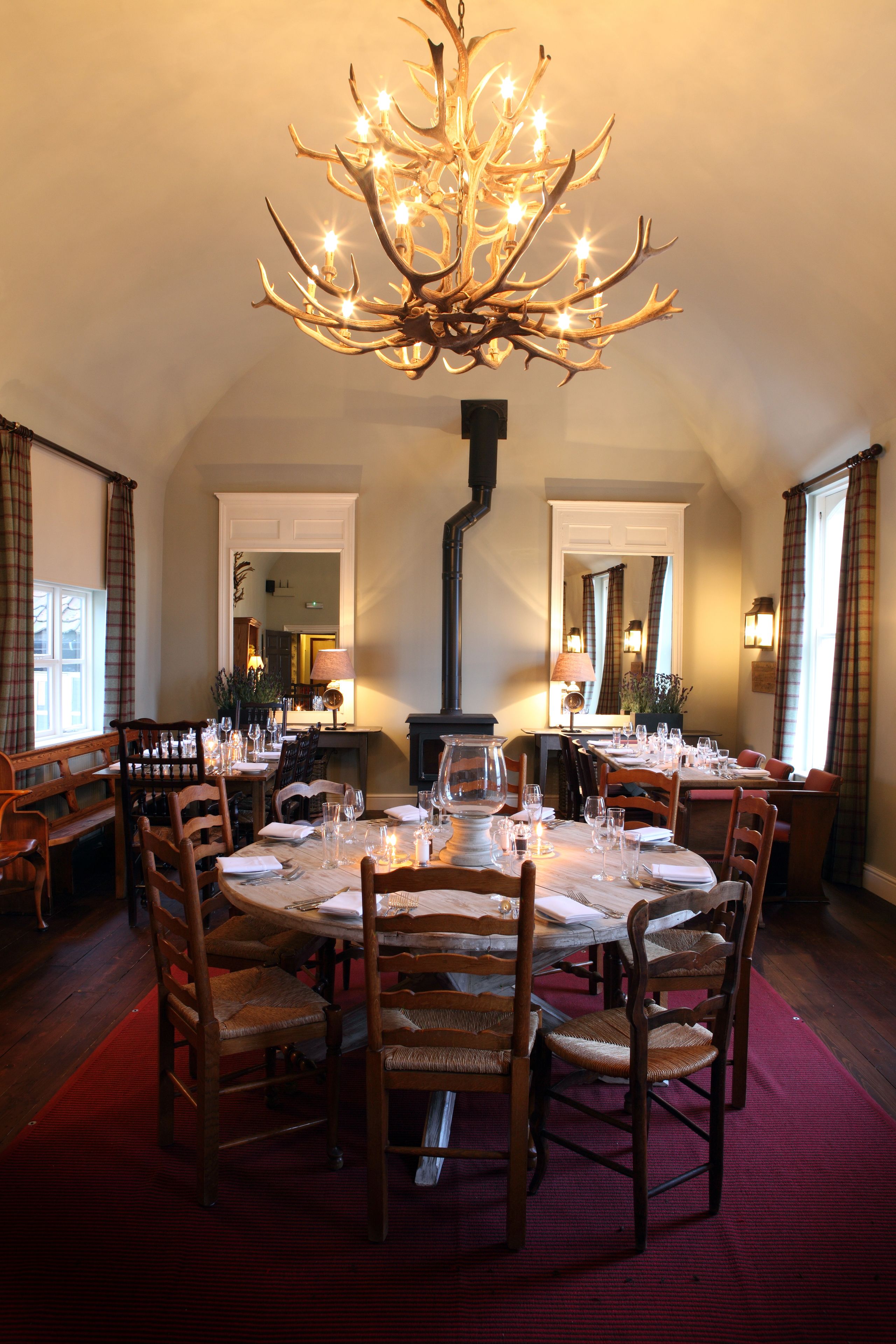 Comedor con una mesa redonda dispuesta para seis personas, rodeada de sillas de madera. Un candelabro grande y ornamentado cuelga del techo.