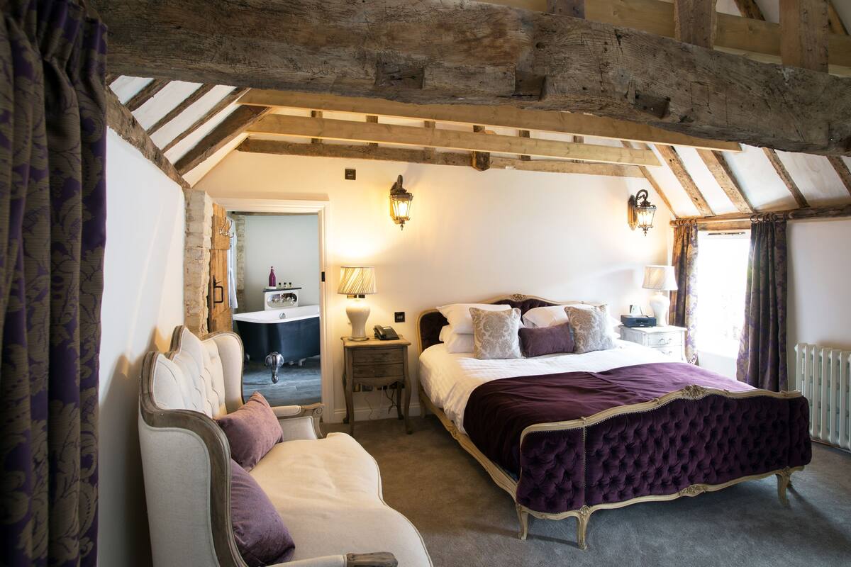 A bedroom with a large bed, a bedside table, a chair, and a wooden ceiling.