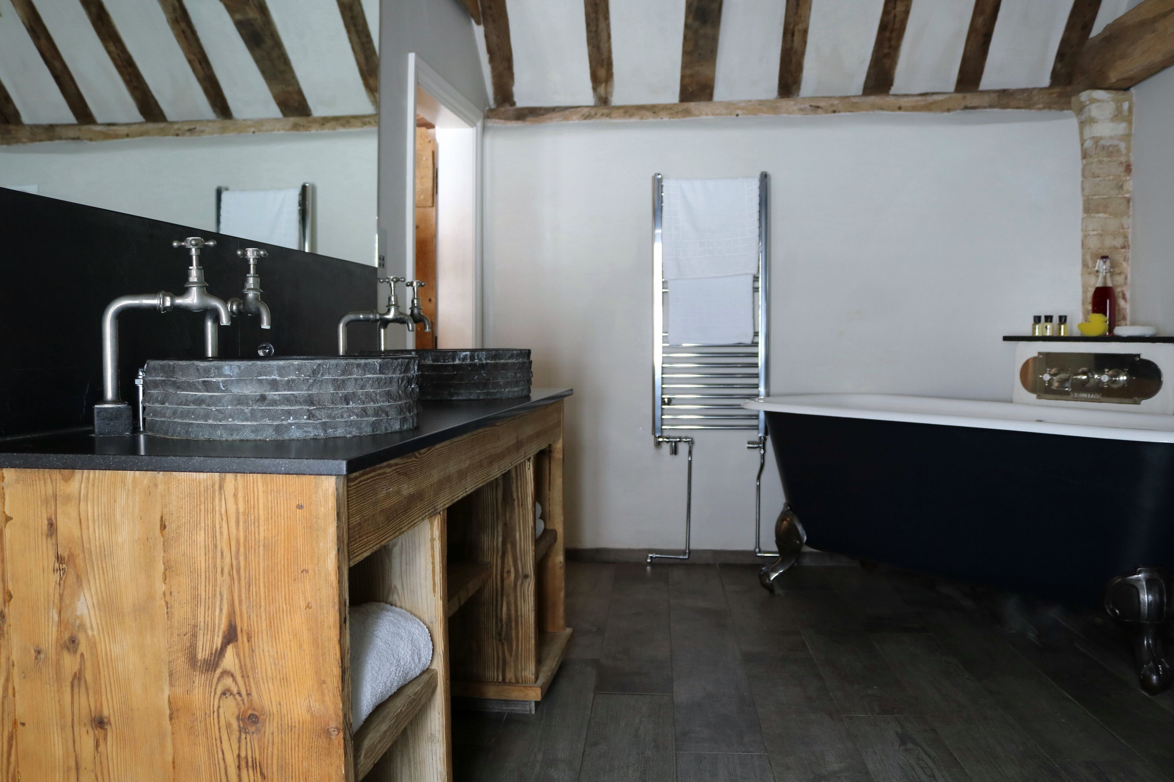 Un baño moderno con tocador de madera, bañera negra y lavamanos blanco.