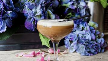 Un cóctel en una copa de martini con espuma, rodeado de pétalos de rosa dispersos sobre una superficie de madera.