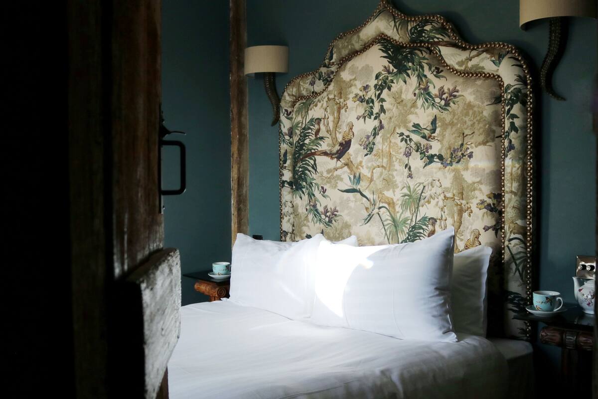 A bed with white linens, a floral headboard, and two wall-mounted lamps.