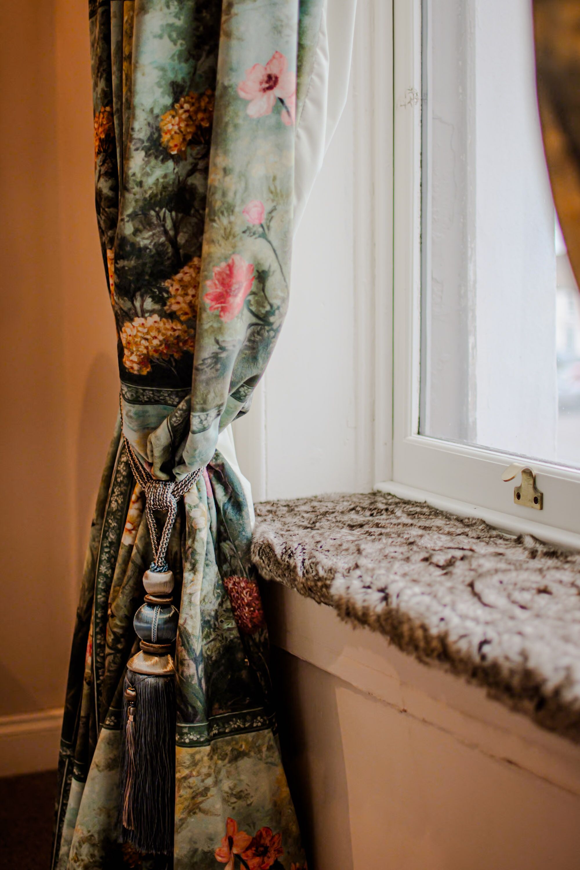 A window with a curtain tied back, revealing a view through the window.