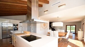 A modern kitchen with a central island, built-in appliances, and a dining area with a white table and chairs.