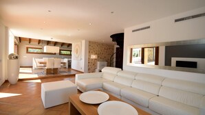 A modern living room with a white sofa, a wooden coffee table, and a dining area in the background.