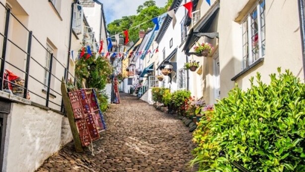 A cobblestone street lined with white buildings, some with balconies and hanging flower baskets. - Putsborough Manor Cottage (4 + Cot) Dogs Tennis Beach Jacuzzi Smart TV wifi (Croyde)