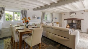 A cozy living room with a wooden dining table, beige sofa, and a stone fireplace. - Putsborough Manor Cottage (4 + Cot) Dogs Tennis Beach Jacuzzi Smart TV wifi (Croyde)