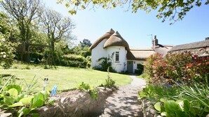 A white house with a thatched roof, surrounded by a garden with a stone wall and a pathway leading to the entrance. - Putsborough Manor Cottage (4 + Cot) Dogs Tennis Beach Jacuzzi Smart TV wifi (Croyde)