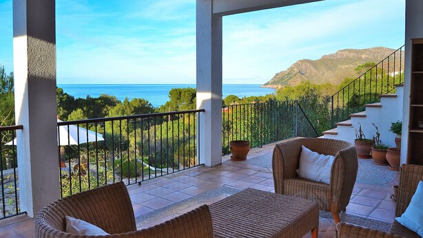 A balcony with wicker furniture, a view of the sea, and a mountainous landscape.