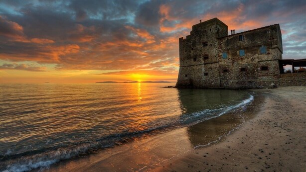 Un edificio histórico de piedra frente al mar al atardecer.