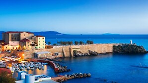 Un pueblo costero con un puerto fortificado, edificios históricos y un faro.