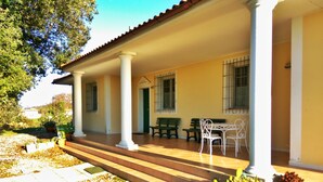 Un patio techado con suelo de baldosas, columnas blancas y mobiliario exterior.