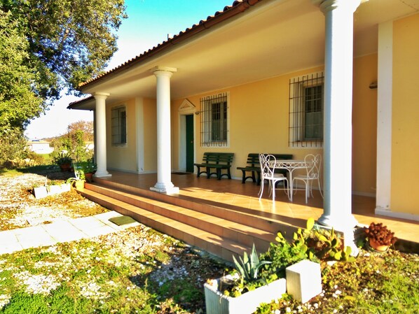 A covered patio with a tiled floor, white columns, and outdoor furniture.