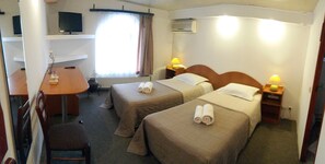 Habitación de hotel con dos camas, un escritorio, una silla, un televisor y una ventana con cortinas.