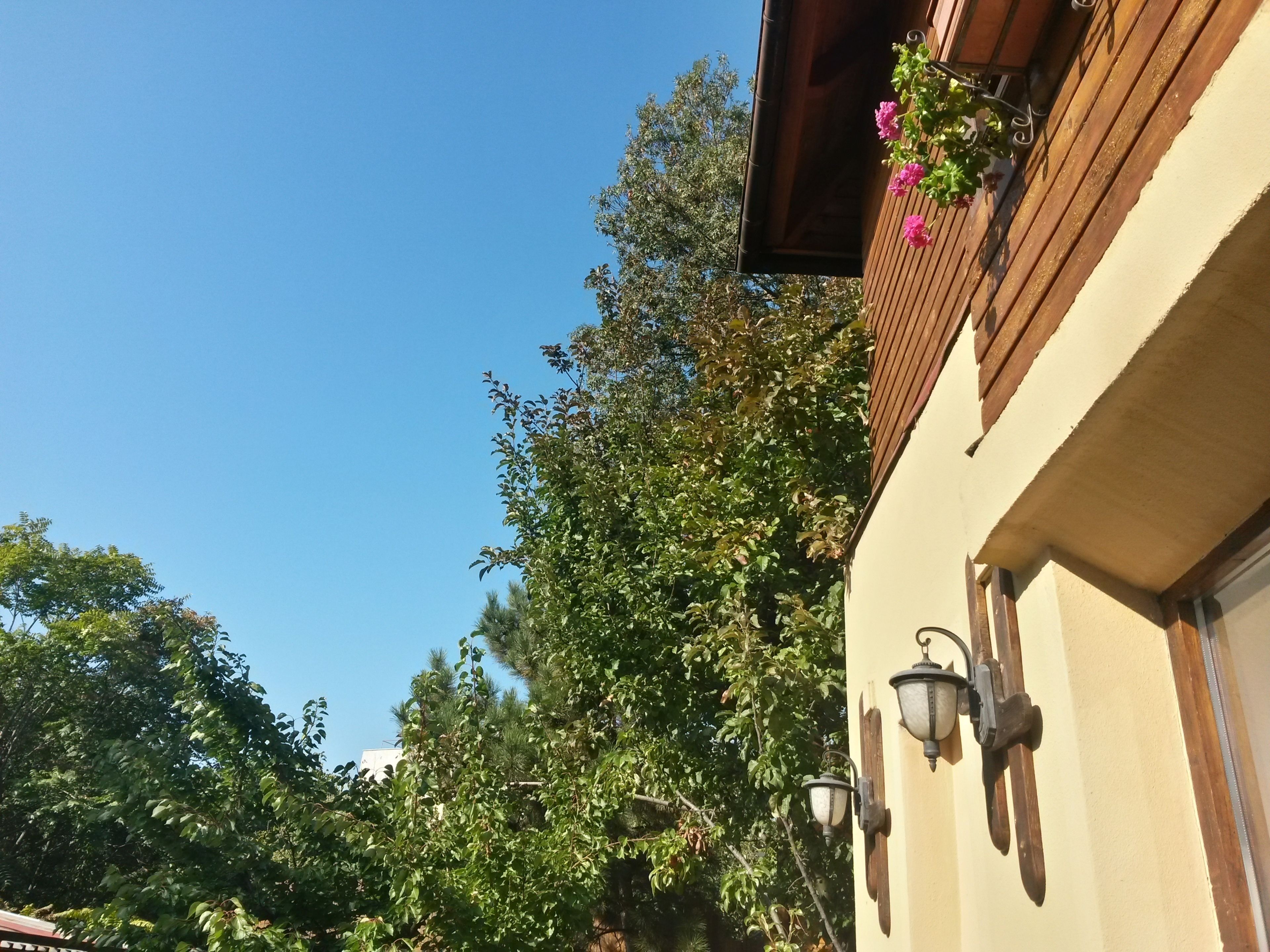 Ein Gebäude mit einem Balkon, der mit Blumen geschmückt ist, einem hölzernen Geländer und einer wandmontierten Leuchte.