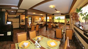 Un restaurant doté de poutres en bois, d’un sol carrelé et de nombreuses tables dressées pour accueillir les clients.
