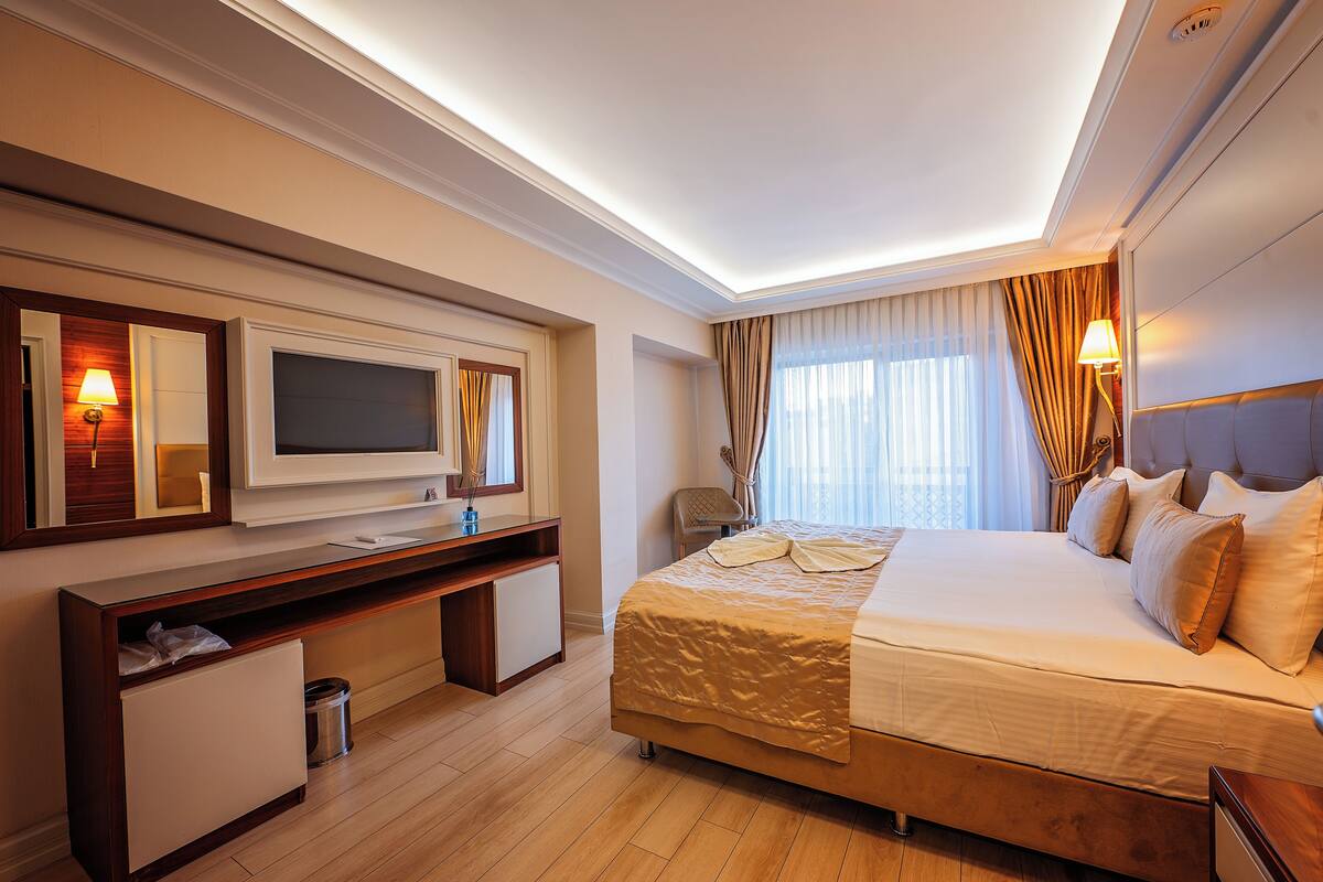 A hotel room with a bed, a desk, a TV, and a window with curtains.