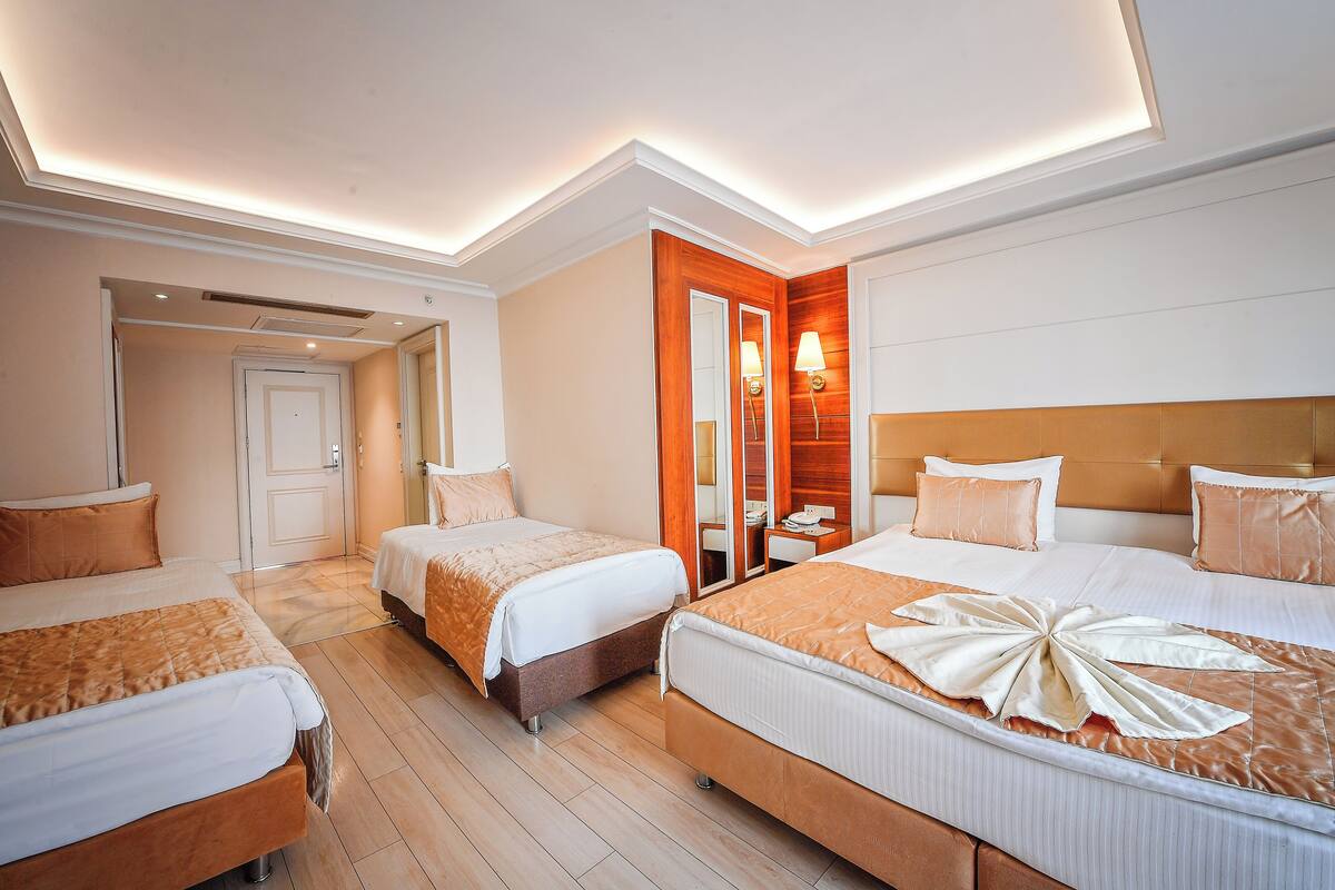 A hotel room with three beds, a wooden headboard, a mirror, and a nightstand with a lamp.