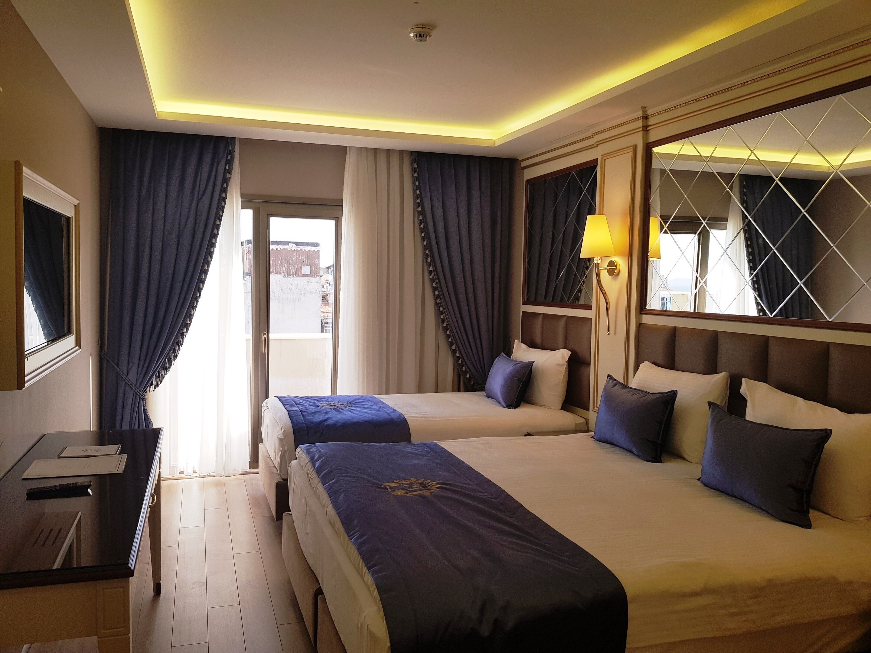 Quarto de hotel com duas camas, uma escrivaninha e uma janela com cortinas.