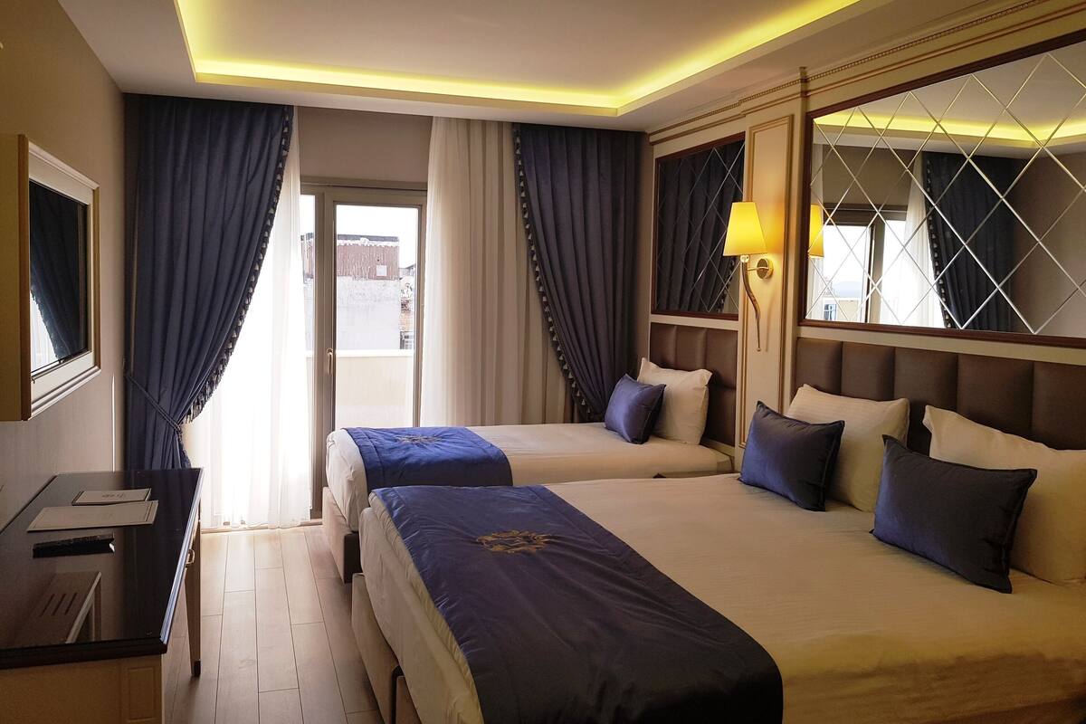Habitación de hotel con dos camas, un escritorio y una ventana con cortinas.
