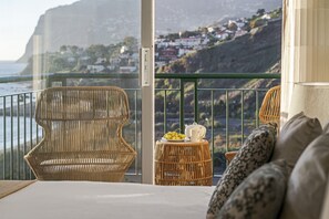Enjoy breathtaking views of the coastline from this room's balcony, featuring a wicker chair and a small table.