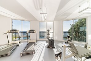 Work out in style with a view of the serene pool and balcony from our fitness room, featuring treadmills, a rowing machine, and a bench press.
