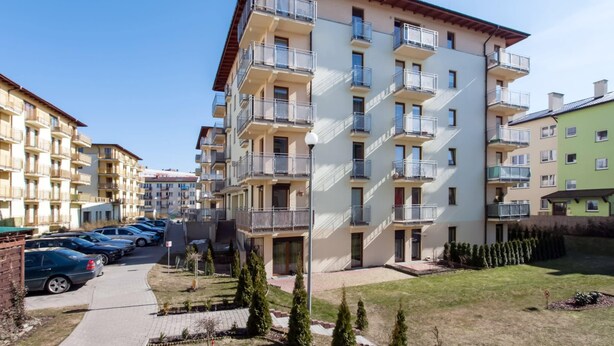 A multi-story residential building with balconies, a parking area, and a small garden.