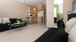 A modern living room with a black sofa, a glass coffee table with a plant, and a kitchen area with a microwave and coffee maker.