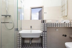 Ein Badezimmer mit Duschkabine aus Glas, einem weißen Waschbecken und einer gefliesten Rückwand.