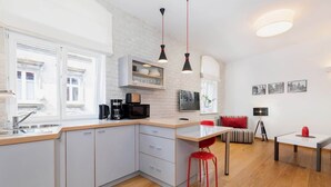 Une cuisine moderne dotée d’un grand îlot central, de meubles blancs et d’une chaise rouge. On y trouve également un coin repas avec une table et une lampe.