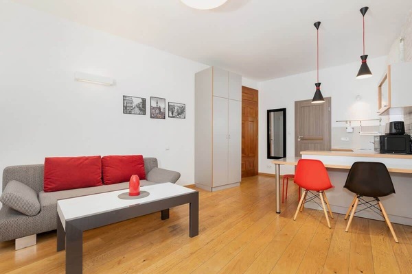 A cozy living room featuring a modern red sofa and a small coffee table. The room has light-colored wooden floors and is decorated with simple black-and-white artwork on the walls.