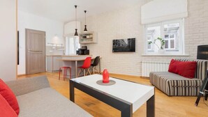 Un salon moderne avec un canapé, une table basse et un coin repas comprenant des chaises, et une cuisine en arrière-plan.