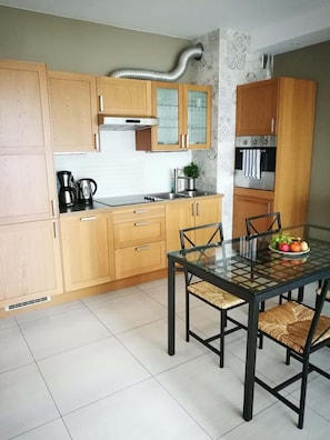 Une cuisine moderne avec des meubles en bois, un four en acier inoxydable et une table à manger en verre, accompagnée de chaises.
