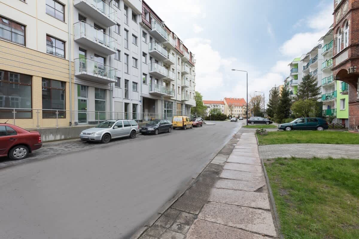 Un immeuble résidentiel à plusieurs étages, doté de balcons, avec des voitures garées et un trottoir.