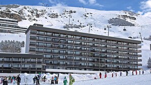 A multi-story hotel with a modern architectural design, located in a snowy mountainous area. - Ski-in/Ski-out Apartment for 6 in La Croisette with South-Facing Balcony (Les Menuires)