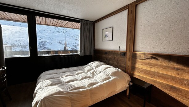 A bedroom with a large bed, wooden headboard, a window with a view of a snowy landscape, and a framed picture on the wall. - Ski-in/Ski-out Apartment for 6 in La Croisette with South-Facing Balcony (Les Menuires)