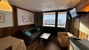 A cozy room with a sofa, a small table, a TV, and a view of a snowy landscape. - Ski-in/Ski-out Apartment for 6 in La Croisette with South-Facing Balcony (Les Menuires)