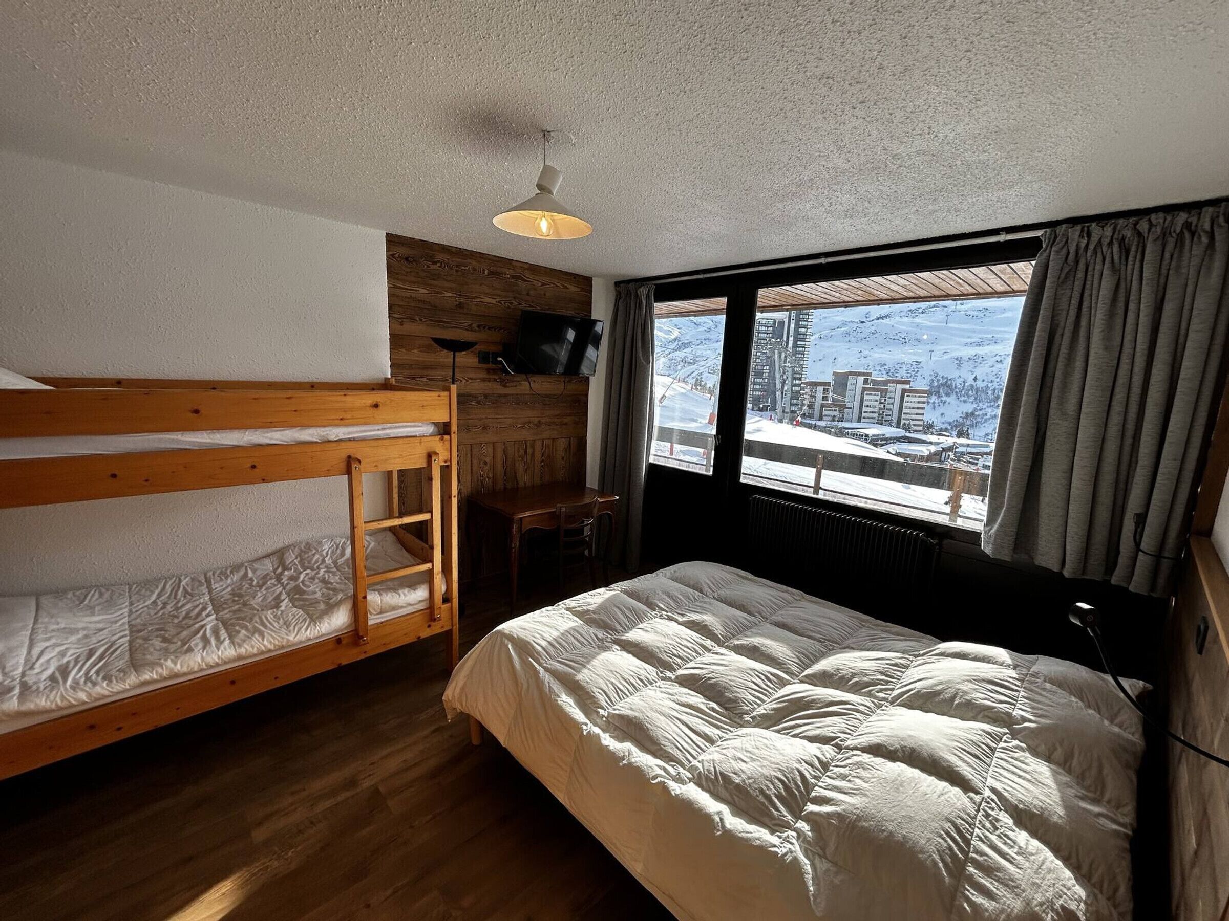 A room with a bunk bed, a single bed, a desk, and a TV.