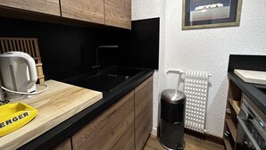 A modern kitchen with wooden cabinets, a black countertop, a sink, a kettle, a trash can, and a radiator. - Ski-in/Ski-out Apartment for 6 in La Croisette with South-Facing Balcony (Les Menuires)