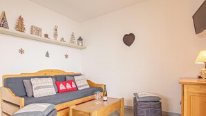 Una sala de estar acogedora con un sofá de madera, una mesita, un televisor y un estante con adornos navideños.