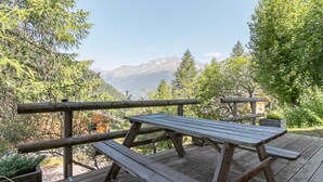 Una terraza de madera con mesas de picnic con vistas a un paisaje montañoso.