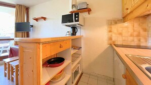 Una cucina compatta con mobili in legno, un forno a microonde, una macchina da caffè e un piccolo angolo ristoro con tavolo e sedie.