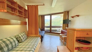 Una stanza accogliente con un divano a quadri, un mobiletto in legno con stoviglie, un tavolo da pranzo con sedie e un'ampia finestra con vista sull'esterno.