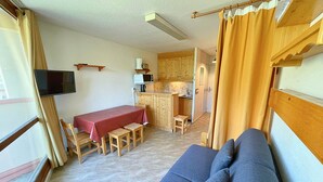 Un ambiente compatto con divano, tavolo da pranzo con sedie, angolo cottura e televisione a parete.